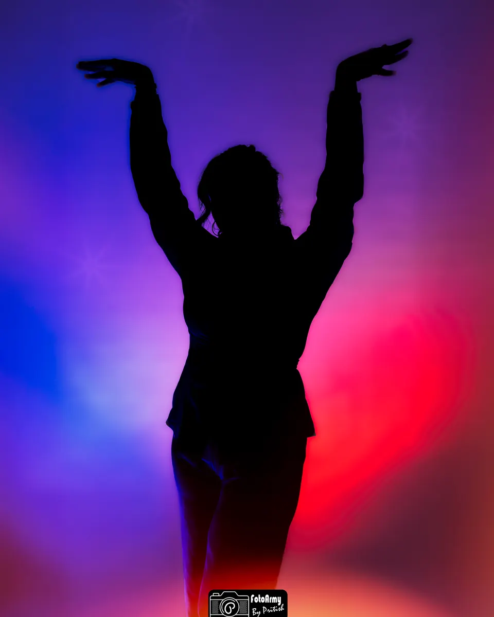 Silhouetportret met opgeheven armen en kleurrijk tegenlicht