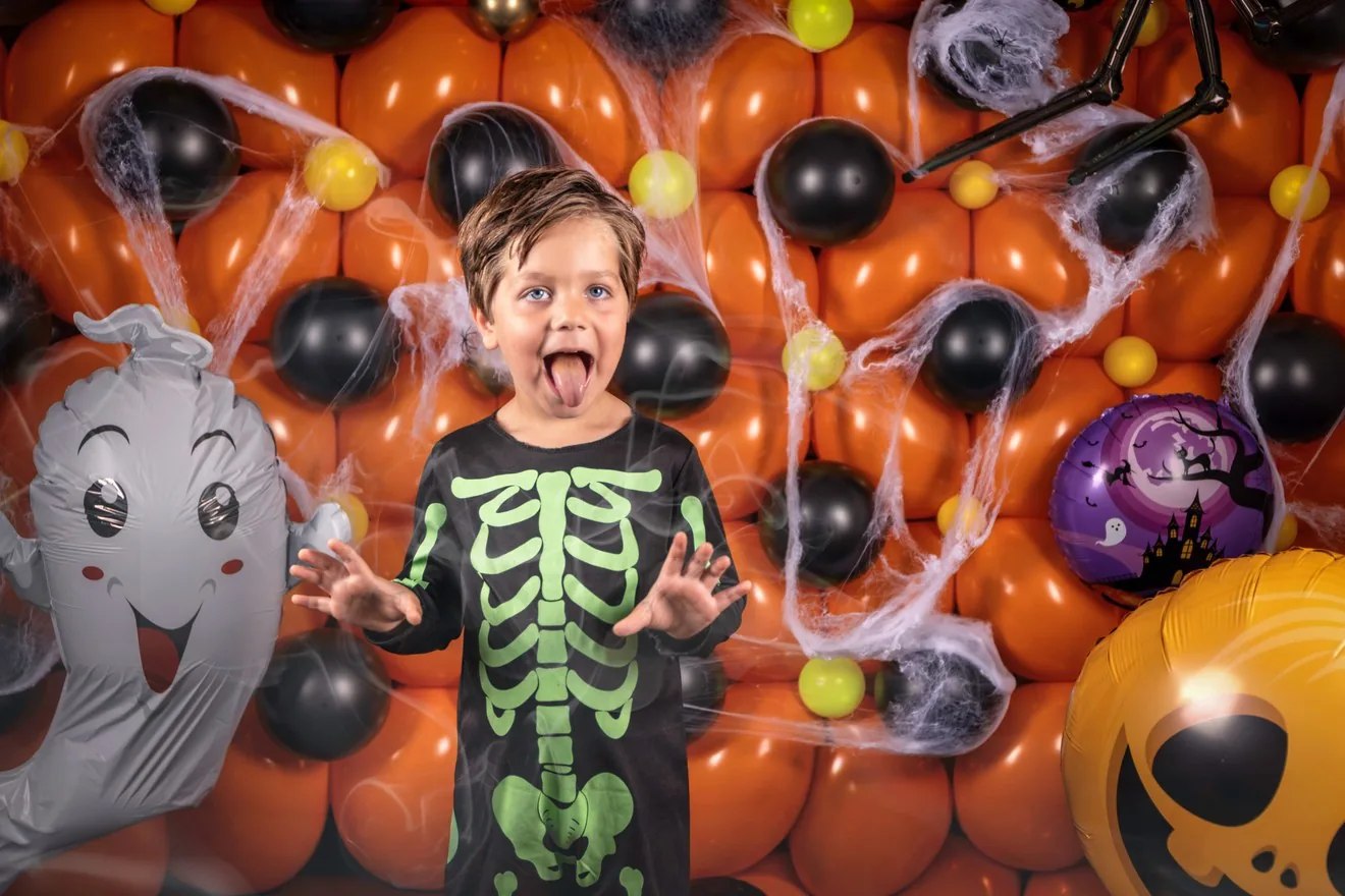 Kind in Halloween-kostuum voor de oranje ballonnenwand met spinnenweb en pompoen-versiering van de Halloween mini fotoshoot bij FotoArmy