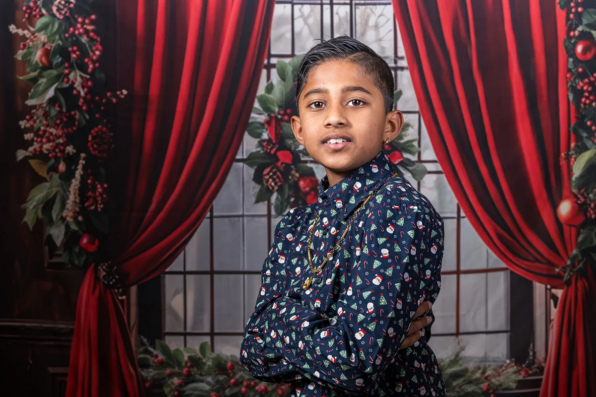 Kerstportret van een kind in een donker overhemd voor rode gordijnen