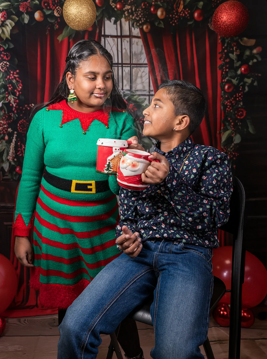 Twee kinderen met kerstmokken in een rood en goud versierde setting